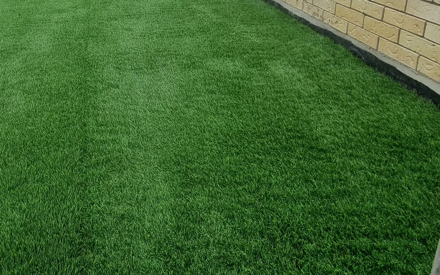 Artificial turf laid tight against a timber fence with a fresh garden edge